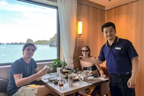 A luxurious cruise ship sailing through the iconic limestone karsts of Halong Bay at sunset