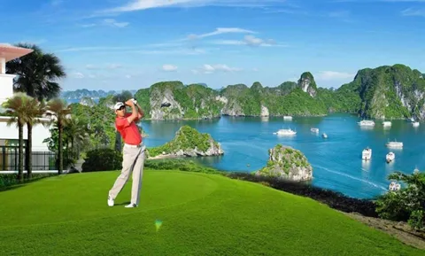 An aerial view of a green golf course with a lake and mountains in the background, showcasing Vietnam's diverse golfing lands