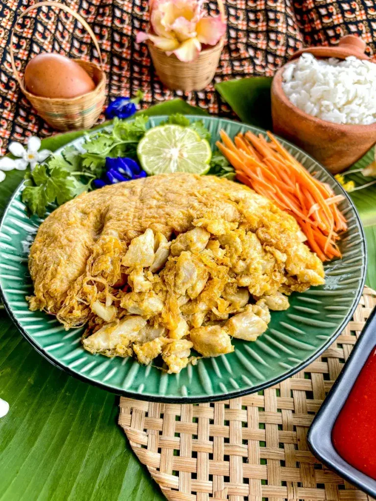 A close-up of a golden-brown Thai crab omelette filled with generous chunks of crab meat, served on a plate.
