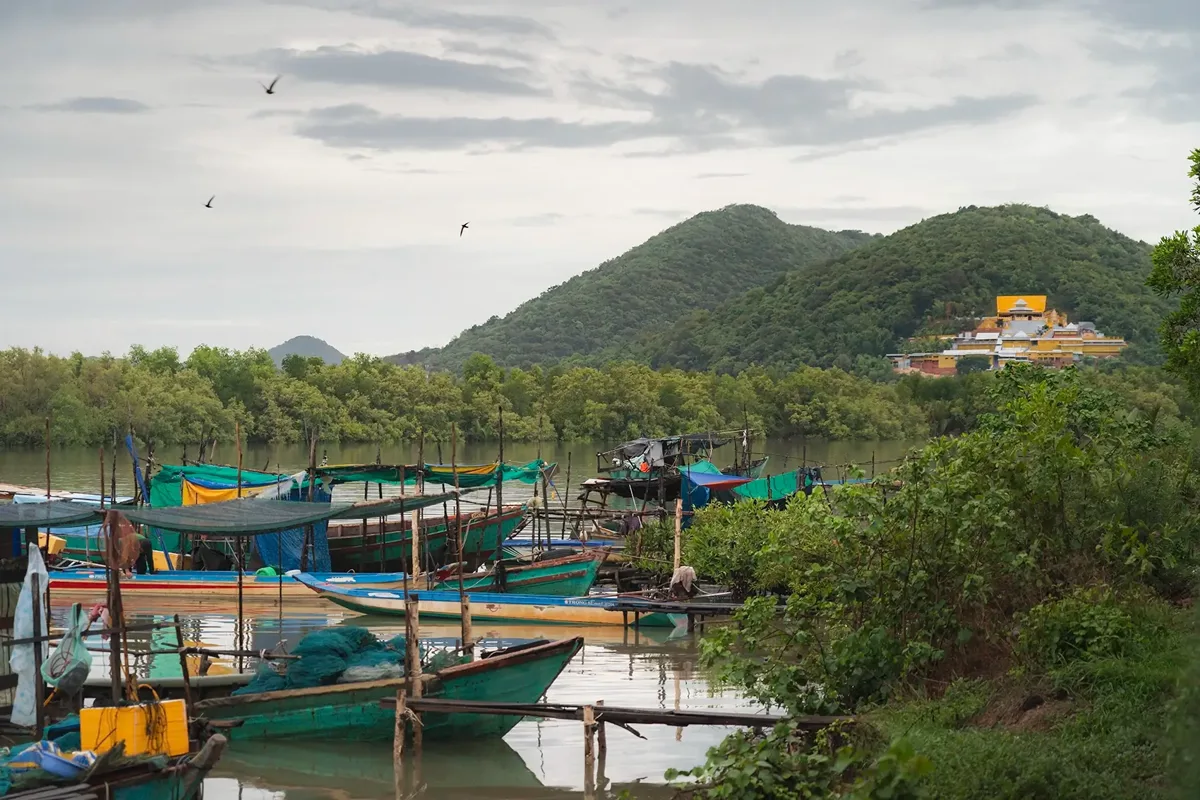Panoramic view of Ha Tien's coastline with fishing boats, limestone karsts, and lush greenery under a clear sky, capturing it