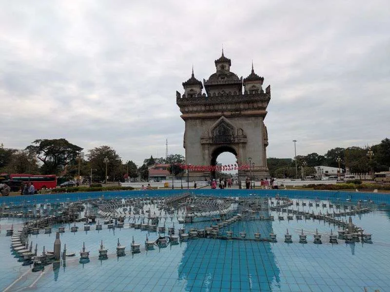 Panoramic view of Patuxai Monument in Vientiane, Laos, with lush green trees and clear blue sky, capturing the city's blend o