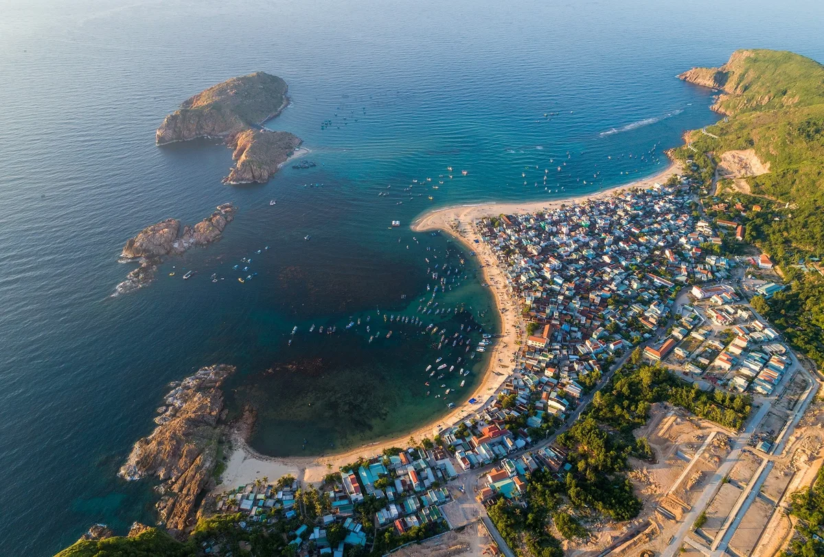 Panoramic view of Quy Nhon coastline with pristine beaches, turquoise waters, and lush green mountains under a clear sky.