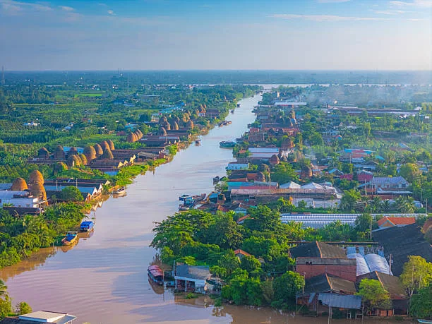 A traditional wooden sampan boat navigating a narrow, lush green canal in the Mekong Delta, Vinh Long, Vietnam, surrounded by